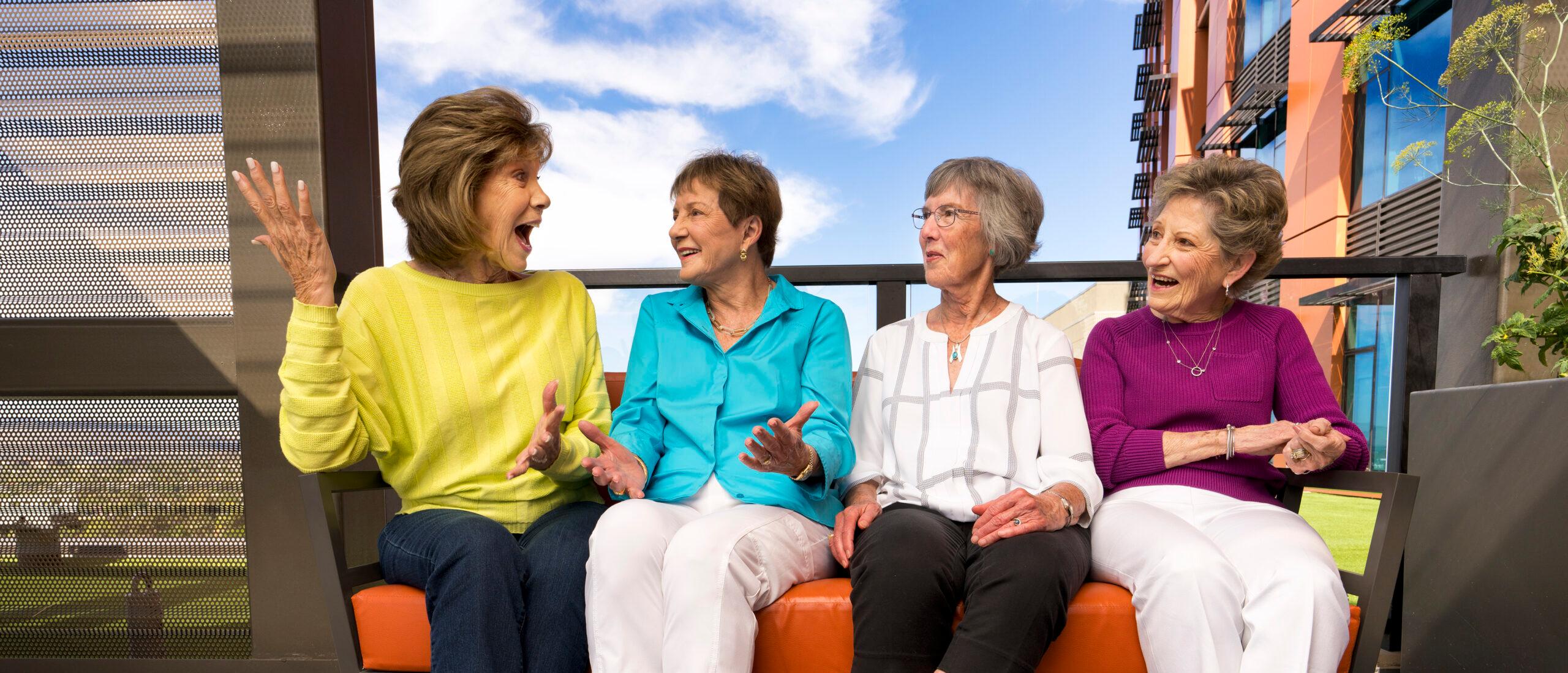 Four friends laugh and talk while sitting on a bench.