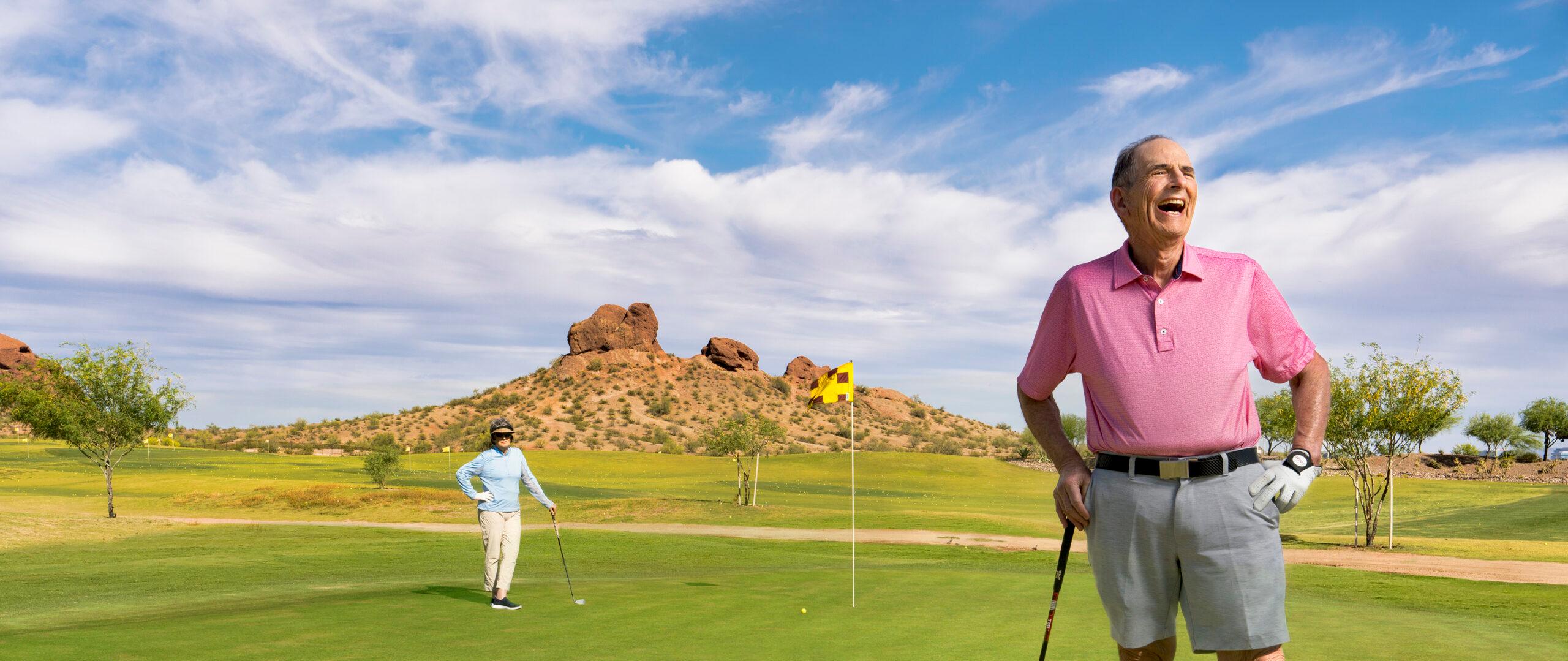 Two happy older adults stand on a golf course.